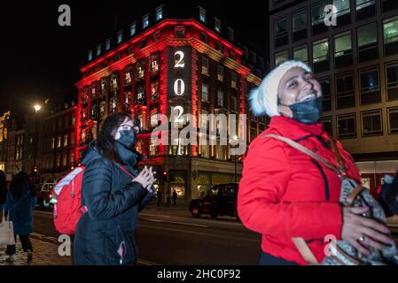 London, Großbritannien. 22. Dezember 2021. Eine Frau (fast mit Gesichtsmaske) geht an den Weihnachtsdekorationen vor Fortnum & Mason auf Piccadilly vorbei, die in Form eines Adventskalenders entstehen. Da die Coronavirus-Pandemie weiter anhält und sich die neue Omicron-Variante als hochgradig übertragbar erweist, wurden im letzten 24-Stunden-Zeitraum 106.122 Fälle registriert, das erste Mal seit Beginn der Pandemie über 100.000. Kredit: Stephen Chung / Alamy Live Nachrichten Stockfoto