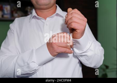 Mann, der ein Manschettenglied am Hemd befestigt. Der Bräutigam schließt Manschettenknöpfe am Hemd Stockfoto