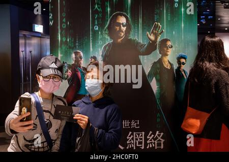 Hongkong, China. 22nd Dez 2021. Kinobesucher machen ein Selfie vor einem Filmbanner von Warner Bros. Picters für die Premiere des Films Matrix Resurrections, gespielt von Keanu Reeves, in einem Kino in Hongkong. Kredit: SOPA Images Limited/Alamy Live Nachrichten Stockfoto