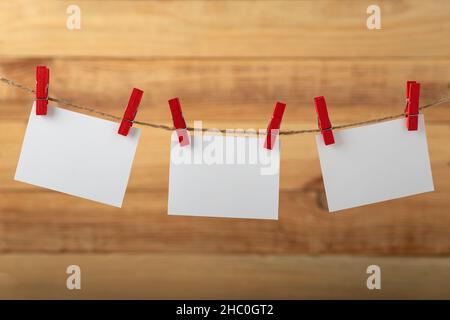 Drei leere weiße Papierkarten, die mit Wäscheklammern auf einem Holzhintergrund an einem Seil-Schnur hängen. Speicherplatz kopieren. Stockfoto