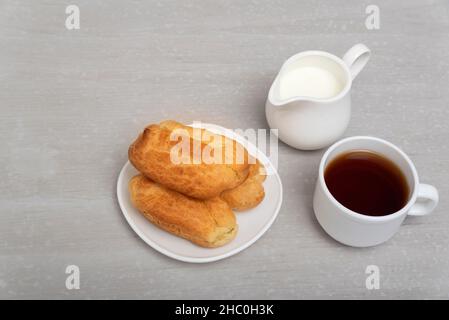 Hausgemachte Lair, Kaffee und Milch. Traditionelle französische Küche. Profiterolen auf der Untertasse. Grauer Hintergrund. Stockfoto