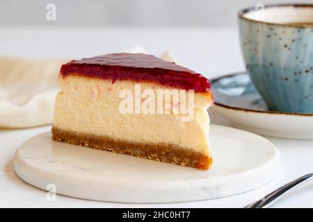 Käsekuchen auf weißem Hintergrund. Griechisches Dessert-Konzept. Teller mit geschnittenem Käsekuchen. Käsekuchen mit Himbeer-Gel-Füllung. Mediterrane Bäckerei. Stockfoto