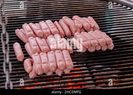 Prozess des Grillens von frischen Fleischwürsten auf einem großen runden Grill Stockfoto