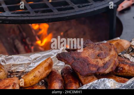 Prozess des Kochens von Steaks, Würstchen und Kartoffeln in Folie auf dem Brazier Stockfoto