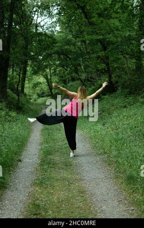 Blondine geht durch den Wald, trägt ein türkisfarbenes T-Shirt. Das Mädchen tanzt Stockfoto