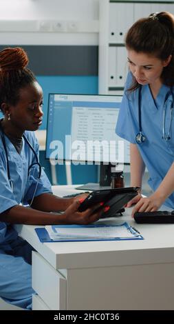 Medizinisches Team, das mit digitalen Tablets für das Gesundheitssystem in der Arztpraxis arbeitet. Gesundheitsassistenten sprechen, während sie das Display für Untersuchung und Behandlung betrachten. Krankenschwestern im Schrank Stockfoto