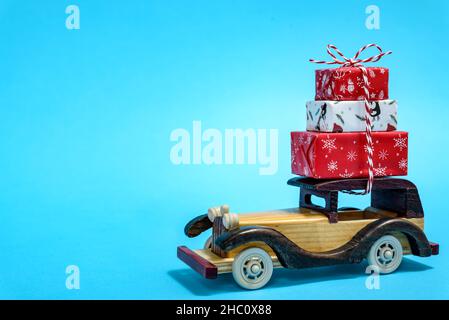 Spielzeugauto aus Holz mit Geschenkboxen auf dem Dach auf blauem Hintergrund. Konzept der Feier von Weihnachten und Neujahr. Stockfoto