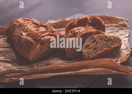 Baguette aus Buchweizenmehl ohne Hefe auf schwarzem Hintergrund, Scheiben Brotscheiben auf Pergamentpapier. Stockfoto
