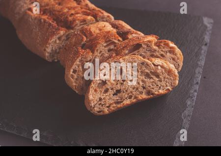 Baguette aus Buchweizenmehl ohne Hefe auf schwarzem Hintergrund, Scheiben Brotscheiben auf Pergamentpapier. Stockfoto