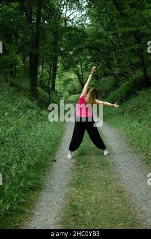 Blondine geht durch den Wald, trägt ein türkisfarbenes T-Shirt. Das Mädchen tanzt Stockfoto