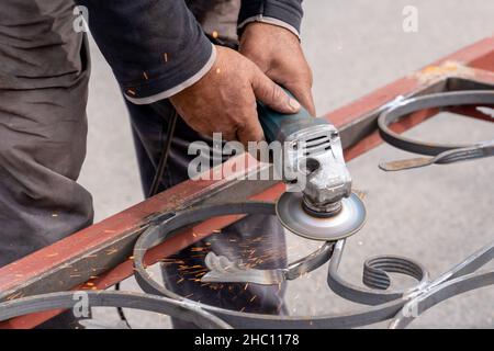 In der Metallwerkstatt mahlt der Mensch Metall mit Winkelschleifer. Funken fliegen an den Seiten. Nahaufnahme der männlichen Hand und des Instruments Stockfoto