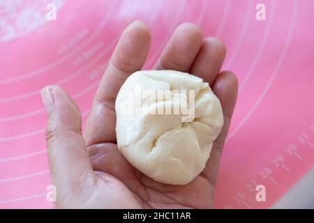 Teig, der zu hausgemachten Roti oder gedünsteten Brötchen gerollt wird, wird in die Hand gelegt. Stockfoto