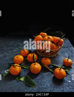 Ein Korb mit Mandarinen auf einem Tisch mit schwarzem Hintergrund Stockfoto