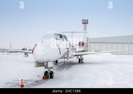 Weißer Luxus-Geschäftsjet in der Nähe des Flugzeughangars bei kaltem Winterwetter Stockfoto