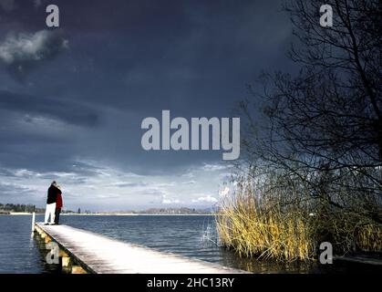 Mann und Frau stehen auf einem kleinen, kurzen Holzsteg, Chiemsee, Bayern, Deutschland Stockfoto