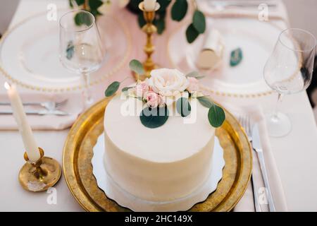 Hochzeitstorte mit einer Rose verziert steht auf einem Goldteller auf dem Tisch Stockfoto