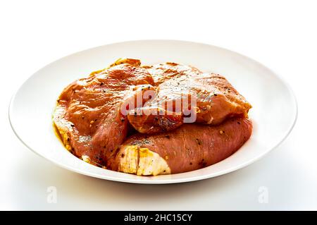 Schweinefleisch in Marinade liegt auf einem weißen Teller auf einem weißen isolierten Hintergrund Stockfoto