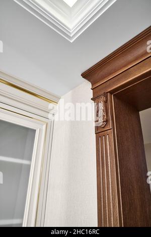 Dekorierter Holzeingang mit geschnitzten Möbelhalterungen und geriffelten Paneele in hellem, geräumigen Zimmer mit moderner LED-Hintergrundbeleuchtung an der Decke Stockfoto