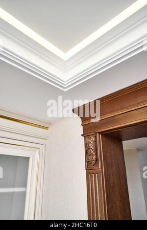 Dekorierter Holzeingang mit geschnitzten Möbelhalterungen und geriffelten Paneele in hellem, geräumigen Zimmer mit moderner LED-Hintergrundbeleuchtung an der Decke Stockfoto