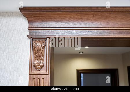 Dekorierter Holzeingang mit geschnitzten Möbelhalterungen und Stuckverzierungen in klassischem Stil in hellem, geräumigen Zimmer in Nahaufnahme Stockfoto