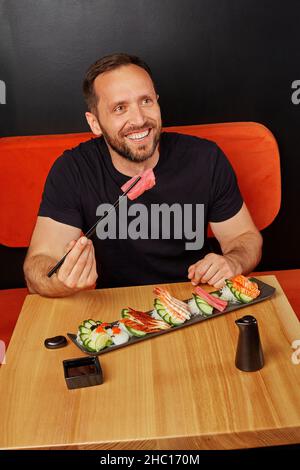 Ein fröhlicher bärtiger Mann genießt es, Sashimi am Tisch im japanischen Restaurant zu essen Stockfoto