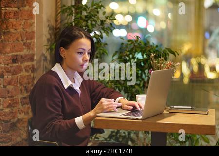 Eine vielbeschäftigte Frau arbeitet im Café am Laptop. Junger afrikanischer Schriftsteller oder Journalist bereitet Artikel im Café vor Stockfoto