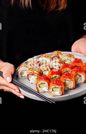 Weibliche Hände halten Essstäbchen und Teller mit Sushi-Rollen mit Lachs und Aal Stockfoto