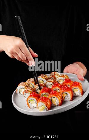 Weibliche Hände verwenden Essstäbchen, um unagi Sushi-Rolle vom Teller zu nehmen Stockfoto