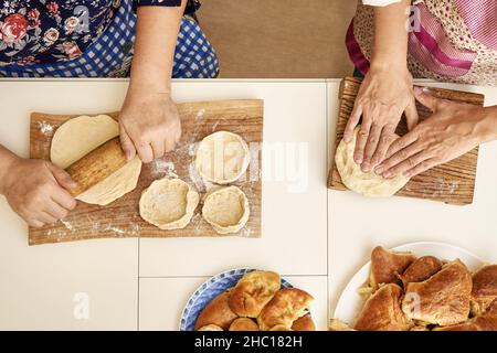 Ältere Frau mit erwachsenen Tochter knetet und rollt rohen Teig und kocht leckere Kuchen am weißen Tisch in der Küche oben aus der Nähe Stockfoto