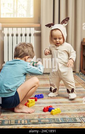 Lustiger kleiner Junge mit Hirsch-Body und älterer Bruder, der auf dem Boden in einem geräumigen Wohnzimmer in der Nähe gebaut wurde Stockfoto