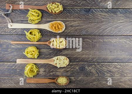 Draufsicht auf Holzlöffel mit verschiedenen Arten von trockener roher Pasta. Brauner Holzhintergrund Stockfoto