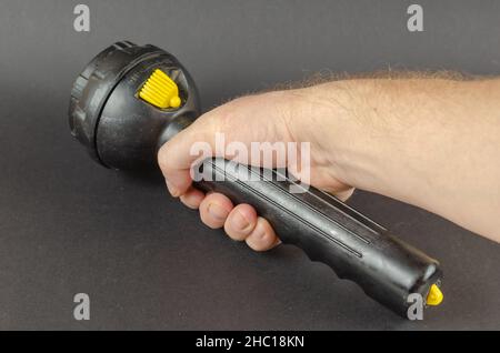 Ein Mann hält eine große schwarze Handtaschenlampe in der Hand. Rechte Hand mit der Laterne vor grauem Hintergrund. Selektiver Fokus. Stockfoto