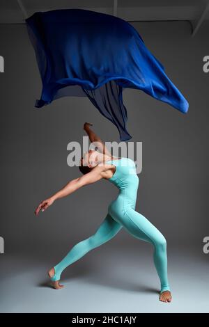 Ballerina tanzt mit Seidenstoff, moderner Balletttänzer in flatterndem, winkenden Tuch, grauer Hintergrund. Stockfoto