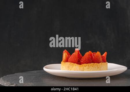 Tartlet mit frischen Erdbeeren auf Untertasse auf schwarzem Hintergrund. Seitenansicht. Obstkuchen. Speicherplatz kopieren, Stockfoto