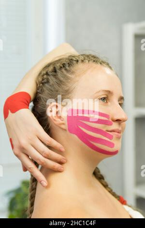 Kinesio-Klebeband auf dem Gesicht einer jungen Frau, um die Haut zu straffen. Facelift Schönheitsverfahren. Physiotherapie und Kinesiologie Stockfoto