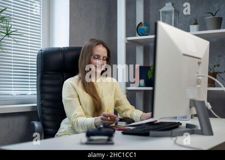 Die Regisseurin sitzt in einem Ledersessel im Büro und liest Dokumente. Chef prüft Vertrag Stockfoto