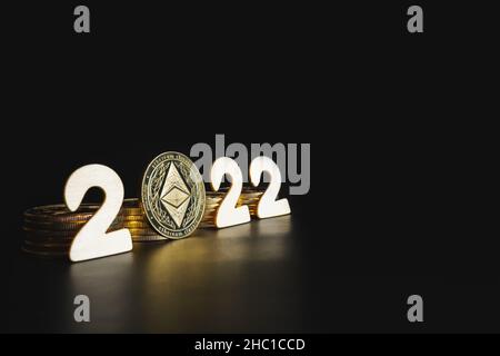 Ethereum in 2022 Preisvorhersage Konzept. Einzelne Äther-Goldmünze neben den weißen Jahreszahlen auf schwarzem Hintergrund mit Platz für Text. Stockfoto