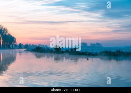 Sonnenaufgang über dem Fluss De Schie und der historischen Hoogevegse Mühle an einem kalten Morgen im südholländischen Stranddorf Noordwijk Stockfoto