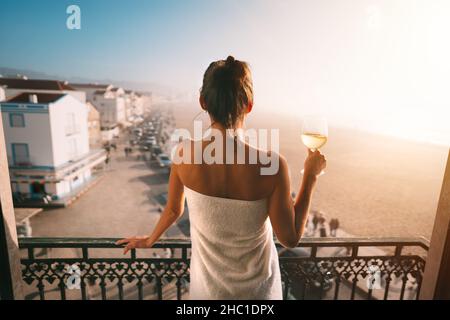 Frau, die auf dem Balkon steht und ein Glas Weißwein in der Hand hält. Genießen Sie das Leben Stockfoto