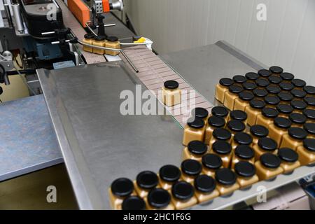 Gläser mit Rahmhonig in einer Verpackungslinie in einer kommerziellen Honigfabrik Stockfoto