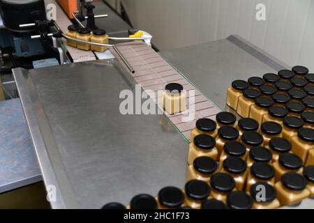 Gläser mit Rahmhonig in einer Verpackungslinie in einer kommerziellen Honigfabrik Stockfoto