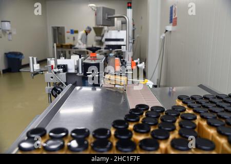 Gläser mit Rahmhonig in einer Verpackungslinie in einer kommerziellen Honigfabrik Stockfoto