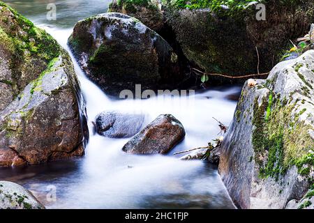 Nahaufnahme einiger Felsen im Fluss, der entlang der Alba-Route in Asturien verläuft.das Foto wurde im horizontalen Format und mit langer Belichtung aufgenommen Stockfoto