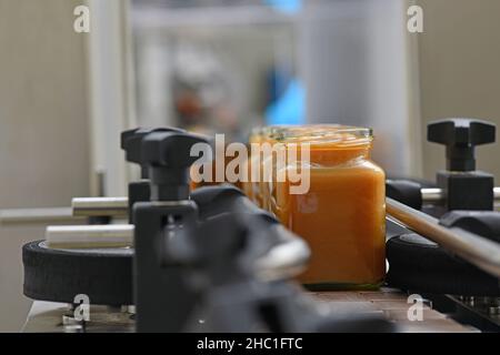 Gläser mit Rahmhonig in einer Verpackungslinie in einer kommerziellen Honigfabrik Stockfoto