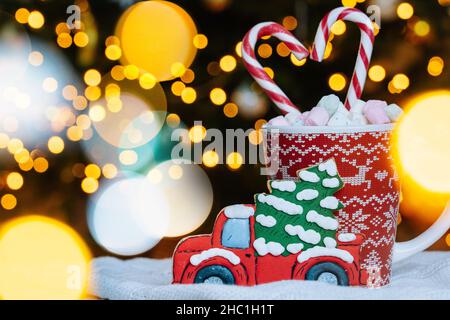Weihnachtskarte mit Lebkuchenkekse, roter Becher mit weihnachtsschmuck auf hellem Bokeh aus dem Weihnachtsbaum und rot gestreiften Weihnachtsgebäck. Weihnachtskandys und Becher mit Marschmeichel auf dem Hintergrund Stockfoto