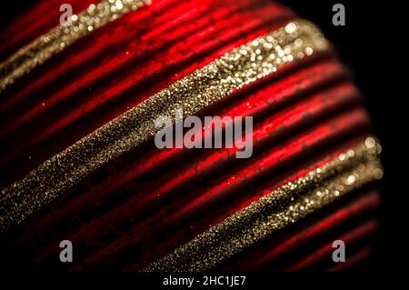 Baumschmuck in Rot und Gold. Nahaufnahme einer rot gemusterten Weihnachtskugel mit Glitzerstreifen. Stockfoto