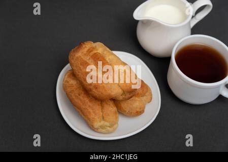 Eclairs für Tee mit Milch. Profiterolen auf weißer Untertasse. Traditionelle französische Küche Stockfoto