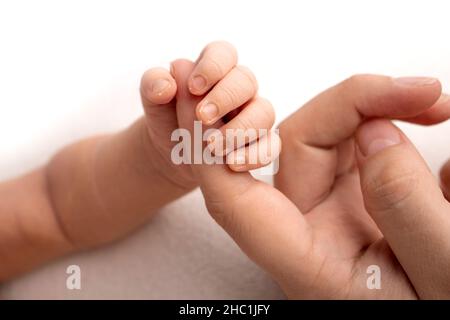 Das neugeborene Baby in einem weißen Schließen hat einen festen Griff auf den Finger der Eltern Stockfoto