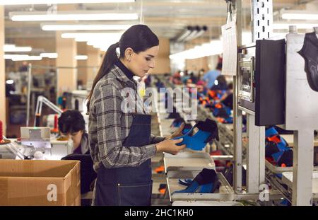 Schuhfabrikarbeiter steht in der Nähwerkstatt und überprüft die Qualität der Sneaker-Details Stockfoto