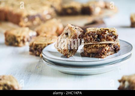 Frisch zubereitete hausgemachte, fudgy Blondies oder Vanillebrownies, die auf einer Untertasse über einem weißen rustikalen Holztisch gestapelt sind. Unscharfer Hintergrund. Stockfoto